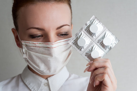 Portrait of a girl in a medical mask. Holding a package of pills in her hand. Close up..