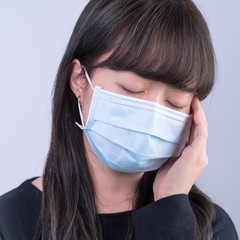 Young woman is feeling dizzy, headache, sick, unwell with wearing a medical blue face mask over the...