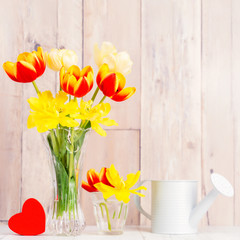 Tulip flower arrangement in glass vase with heart greeting, watering can decor on wooden table...