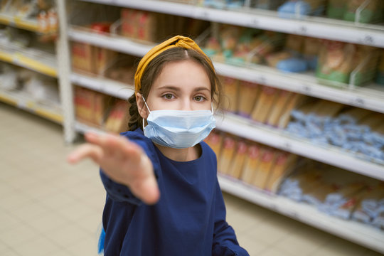 Girl in disposable medical mask shopping in supermarket during an outbreak of coronavirus pneumonia, makes panic stock of products. Empty store shelves, set of products for quarantine self-isolation