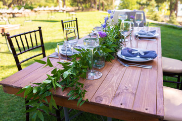 Beautifully decorated wooden table in a summer open-air cafe. Green branch and fresh flowers table decoration