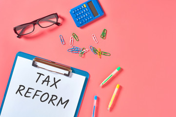 Clipboard with words tax reform near stationery items on pink desk. Business concept