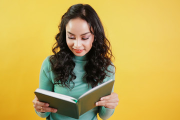 young attractive asian woman reads a book isolated on Yellow background. Intelligent girl reading the book for knowledge.