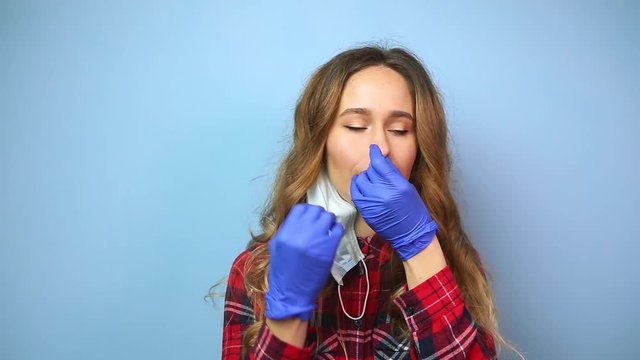 The girl in puts on medical mask on blue background. Violation of sanitary rules for using masks during the coronavirus epidemic. woman touches her face with dirty hands. SARS-CoV-2. Stop COVID-19
