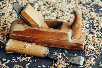 Old hand plane and chisel with wooden shavings on black background. Old woodworking hand tool. Copy, empty space for text