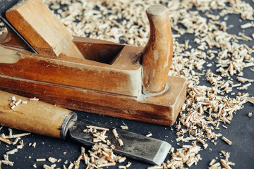 Old hand plane and chisel with wooden shavings on black background. Old woodworking hand tool. Copy, empty space for text