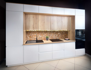 Luxury modern fitted flat design kitchen with surface behind the countertop decorated with wall cross section of tree trunks of cut tree logs, trunks placed together for interior decoration.