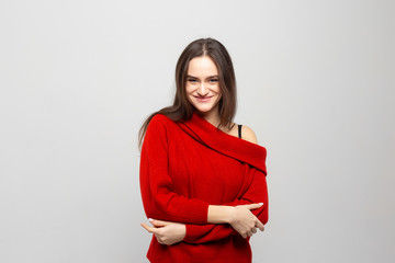 Portrait of a young beautiful woman with a light smile dressed in a red sweater on a light gray background.