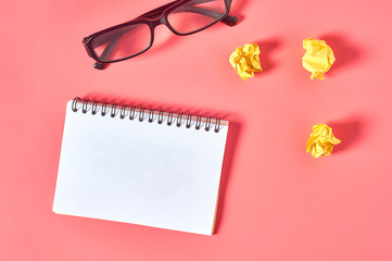 Blank notepad near crumpled paper balls and modern glasses on pink desk. Education or business...
