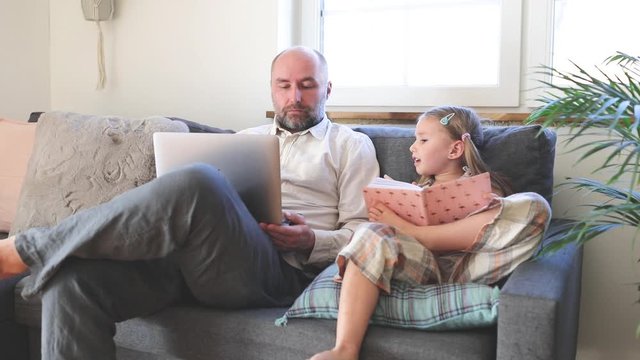 Father using laptop and daughter painting, sitting on sofa at home