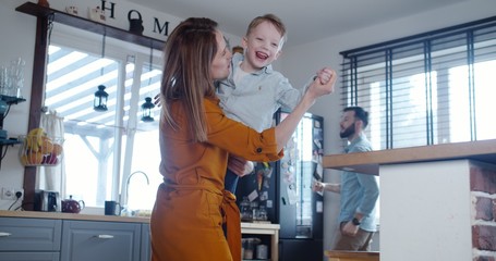 Happy young Caucasian mother and father enjoying playing and dancing together with little cute son at home slow motion.