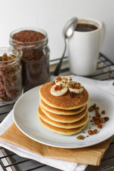 Lush pancakes with banana on a white plate. Coffee in a white cup on the background