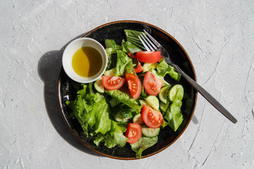 Summer fresh detox salad with tomatoes, cucumber, romaine lettuce and olive oil on grey concrete background. Healthy diet food for vegan or vegetarian, top view