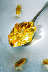 Tablespoon holding omega 3 cod liver oil supplement capsules on a white table top with copy space