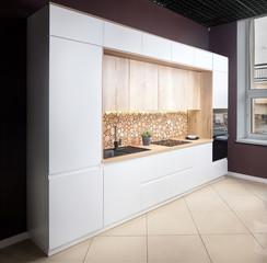 Luxury modern fitted flat design kitchen with surface behind the countertop decorated with wall cross section of tree trunks of cut tree logs, trunks placed together for interior decoration.