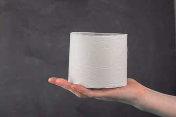 a roll of toilet paper lies on a woman's palm on a gray background