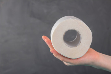 a roll of toilet paper lies on a woman's palm on a gray background