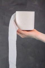 A woman's hand holds a roll of toilet paper on a gray background