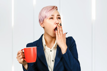Young yawning girl office worker holds cup of a coffee.