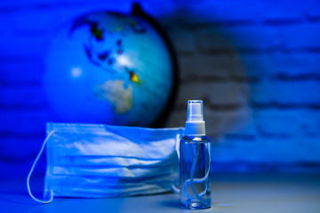 Sanitizer or antiseptic on earth globe behind the mask bakground. Save the planet. Fight the pandemic spreading. COVID-19 and coronavirus