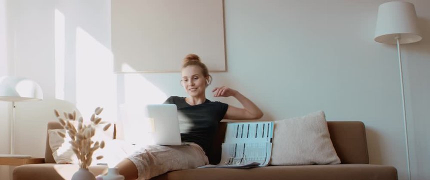 Caucasian female working on a laptop from home, having a video call on a sofa. Stay home, quarantine remote work. Shot on RED Dragon