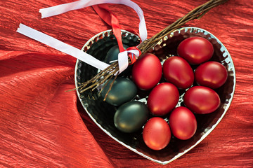 Czech Easter tradition background. Dark red and blue colored eggs on heart shaped dish and wicker whip (Czech: Pomlazka) with ribbons to rejuvenate girls and women at spring to stay young and healthy