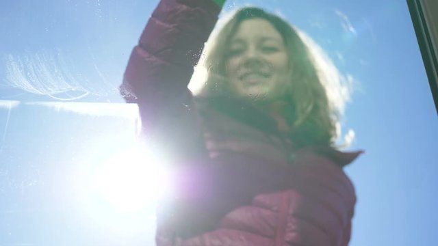 smiling woman in jacket and rubber gloves washes dirty window outside