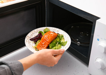 Woman putting plate with food in microwave oven