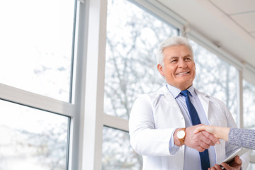 Male doctor with patient shaking hands in clinic