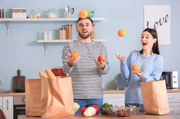 Young couple having fun while unpacking fresh products from market in kitchen