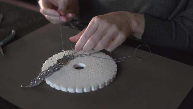 Lifestyle concept, reinvent your life and your job: close-up detail in low angle view of woman hands making macrame knotted bracelet with the fingers knotting the nylon thread on the kumihimo