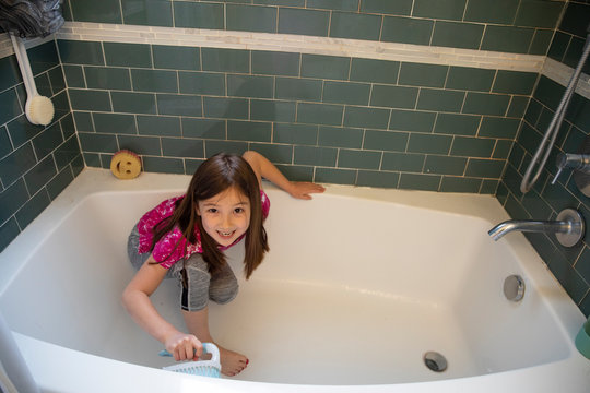 Little girl doing chores, cleaning family bathroom smiling