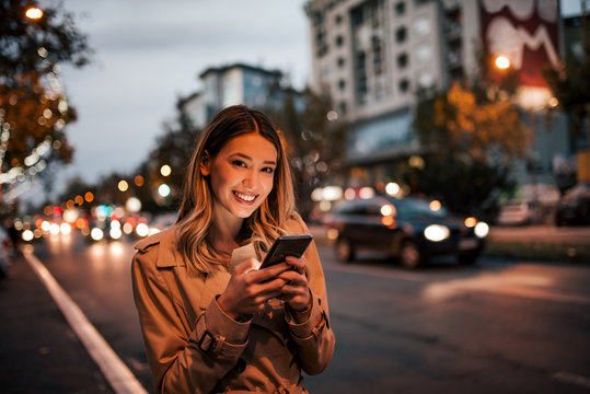 Beautiful woman using smart phone in the city, smiling at camera.