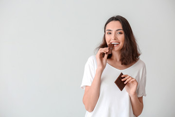 Beautiful young woman eating tasty chocolate on white background