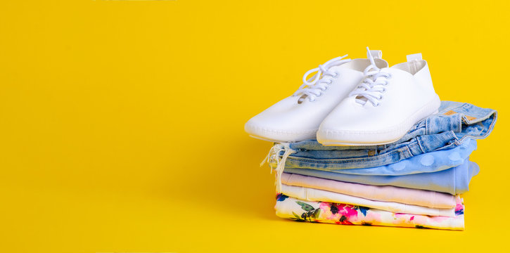 Stack folded colorful clothing summer and white sneakers on yellow background