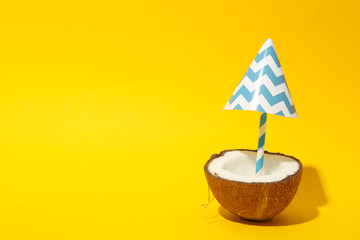Coconut with beach umbrella on yellow background, space for text