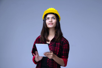 The young woman engineer with yellow safety helmet,using taplet,turn face up and looking for checking her work