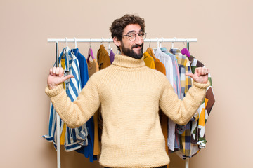 young cool berded man with clothes against flat wall