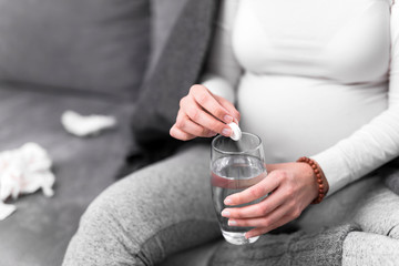 Pregnant woman taking vitamin tablet in a glass of water.