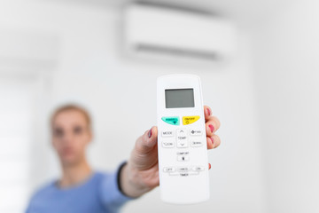 Woman holding a remote of a modern airconditioner unit at home.