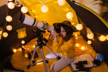 Small girl using telescope at home living room in a tent.