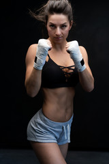 Muscular young woman athlete standing on black background