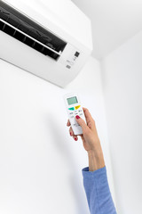 Woman holding a remote of a modern airconditioner unit at home.