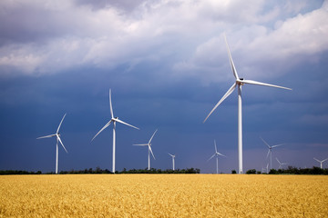 Wind turbines and agricultural field on a summer cloudy day. Energy production, clean and renewable energy.