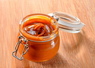 glass jar  with cream  caramel sauce (nice curl pattern) close-up on wooden background 
