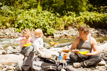 dad with kids on rocky of mountain river and eat