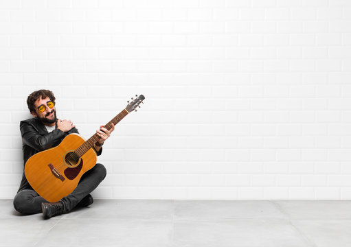 young musician man feeling in love, smiling, cuddling and hugging self, staying single, being selfish and egocentric with a guitar, rock and roll concept