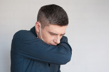 Portrait of coughing european dark hair man in surgery face mask in blue shirt on gray background 