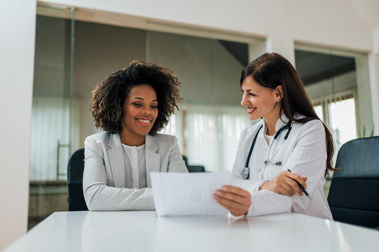 Good News! Smiling Female Patient And Doctor Looking At Paper Document.