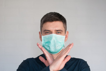 Portrait of european dark hair man in surgery face mask in blue shirt on gray background with crossed palms